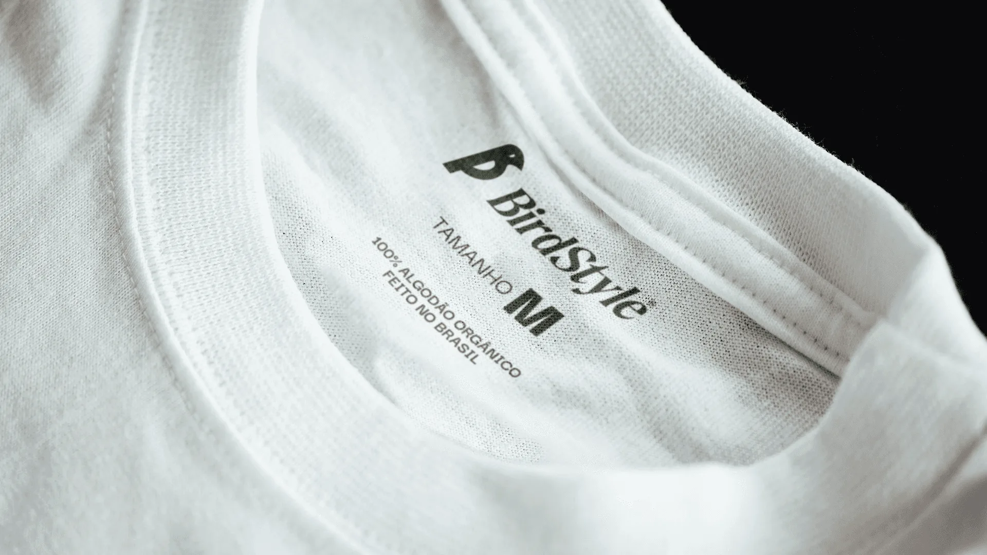 Gola de camiseta branca com etiqueta impressa da BirdStyle indicando tamanho M e 100% algodão orgânico, feito no Brasil