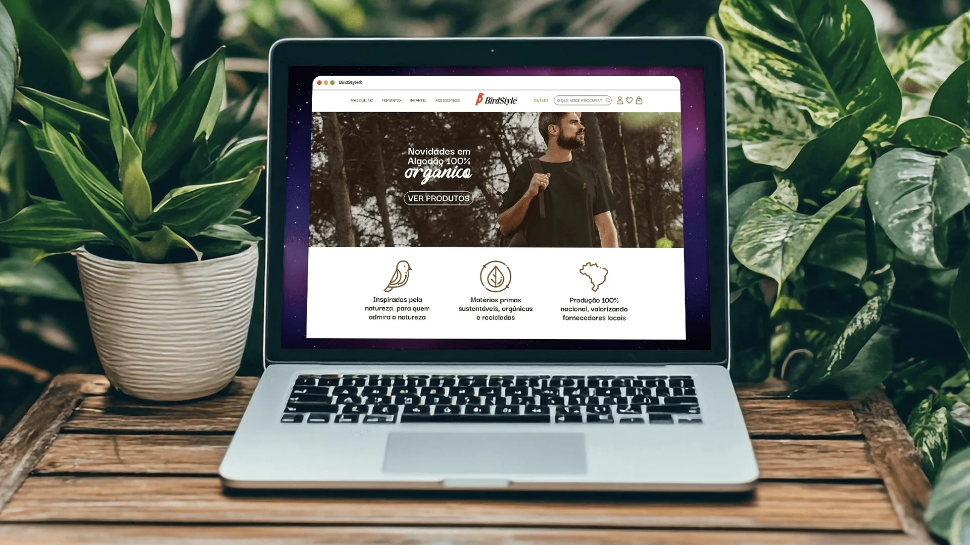 Notebook cercado de plantas exibindo a home do e-commerce da BirdStyle com destaque para novidades em algodão orgânico