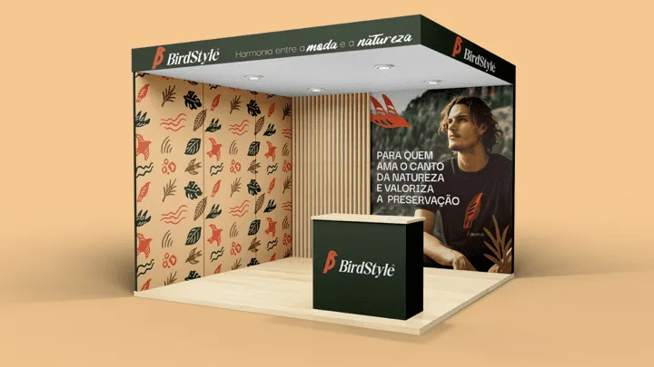 Estande de feira da BirdStyle com painel de grafismos naturais, balcão verde-escuro e painel fotográfico com a frase Para quem ama o canto da natureza e valoriza a preservação